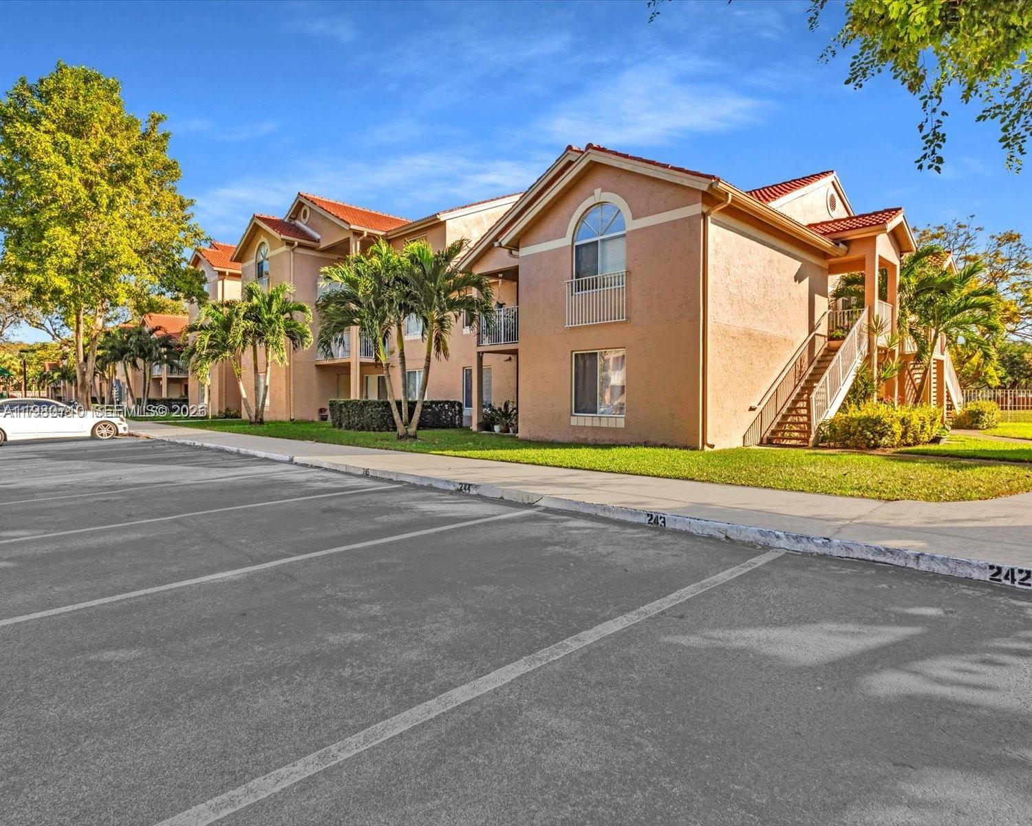 An exterior view of a multi-story apartment complex with red tile roofs and palm trees — 15770 SW 106th Ter # 303, Miami FL 33196, MIAMI, FL
