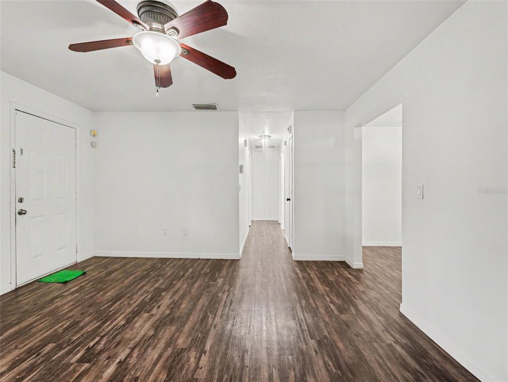 A living room with wood-look flooring, a ceiling fan, and a hallway leading to other rooms — 4042 HOMESTEAD DRIVE, LAKELAND, FL