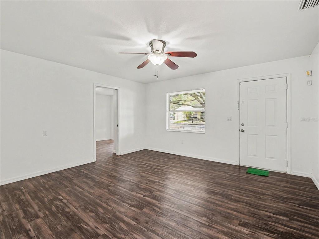 A living room with white walls, dark wood-look flooring, a ceiling fan, and front door — 4042 HOMESTEAD DRIVE, LAKELAND, FL