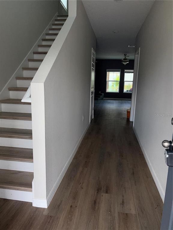 A hallway with wood-look flooring leads past a staircase to a room with dark walls — 11484 BROOK EDGE AVENUE, RIVERVIEW, FL