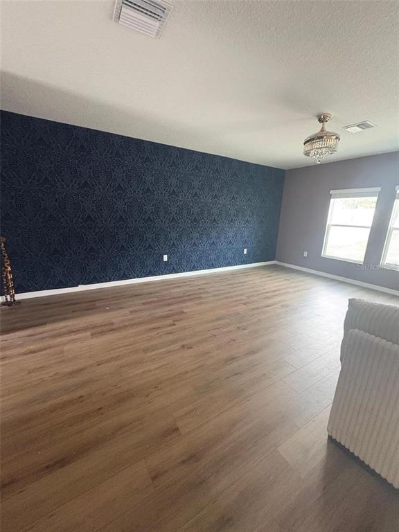A spacious room features wood-look flooring, a dark blue patterned accent wall, and a chandelier — 11484 BROOK EDGE AVENUE, RIVERVIEW, FL