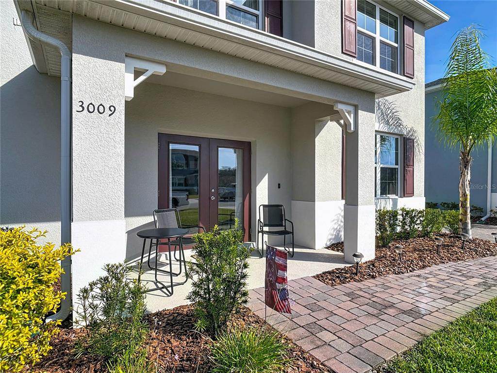 A covered front porch features a small table, two chairs, and a brick walkway — 3009 MELETO BOULEVARD, NEW SMYRNA BEACH, FL