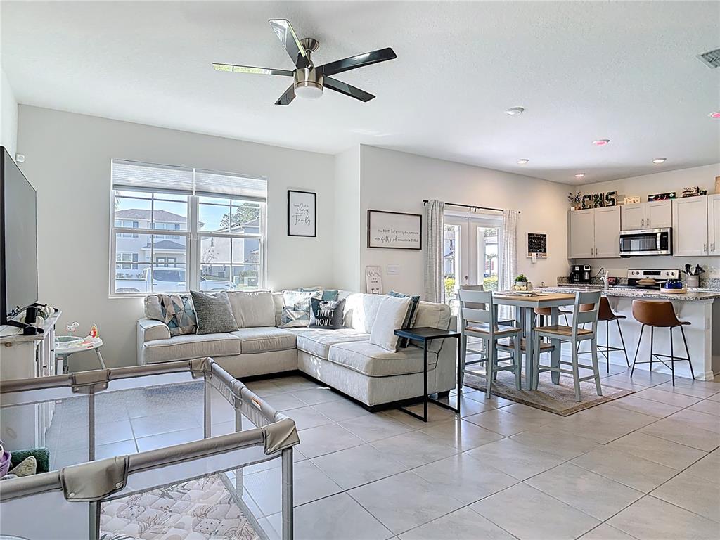 An open-concept living and dining area features light tile flooring, a sectional sofa, and kitchen — 3009 MELETO BOULEVARD, NEW SMYRNA BEACH, FL