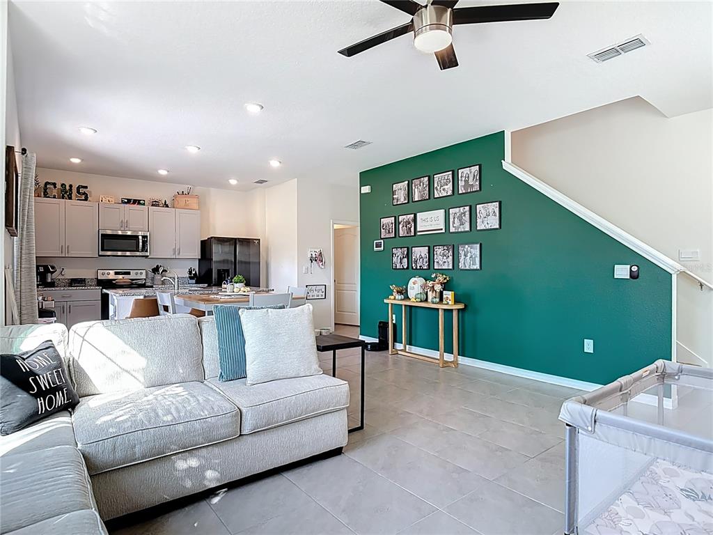 A living room features a grey sofa, a green accent wall with photo frames, and kitchen — 3009 MELETO BOULEVARD, NEW SMYRNA BEACH, FL