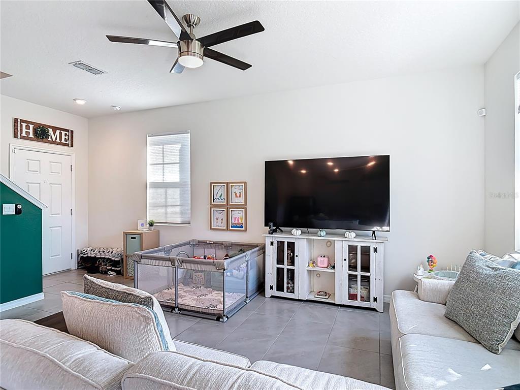A living room features a large television on a white console, a playpen, and tile flooring — 3009 MELETO BOULEVARD, NEW SMYRNA BEACH, FL