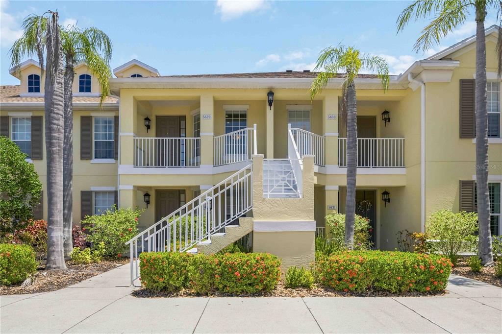 A two-story yellow apartment building features an exterior staircase leading to a second-floor balcony — 5629 KEY LARGO COURT UNIT B06, BRADENTON, FL