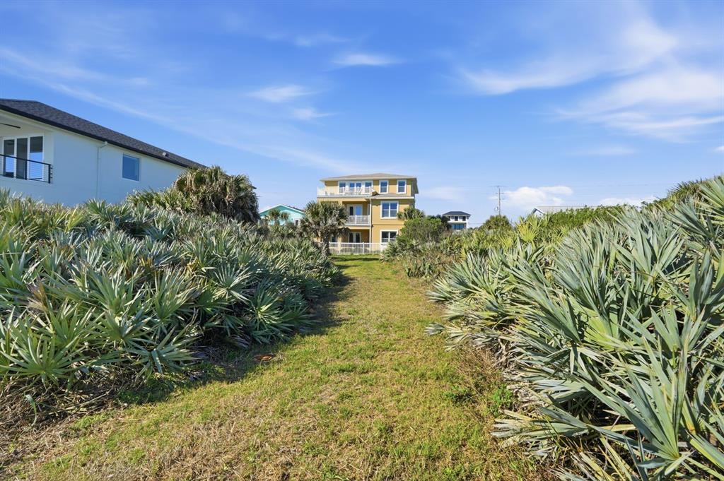 A grassy path leads between dense palmetto bushes toward a multi-story yellow coastal house — 2208 S OCEAN SHORE BOULEVARD, FLAGLER BEACH, FL