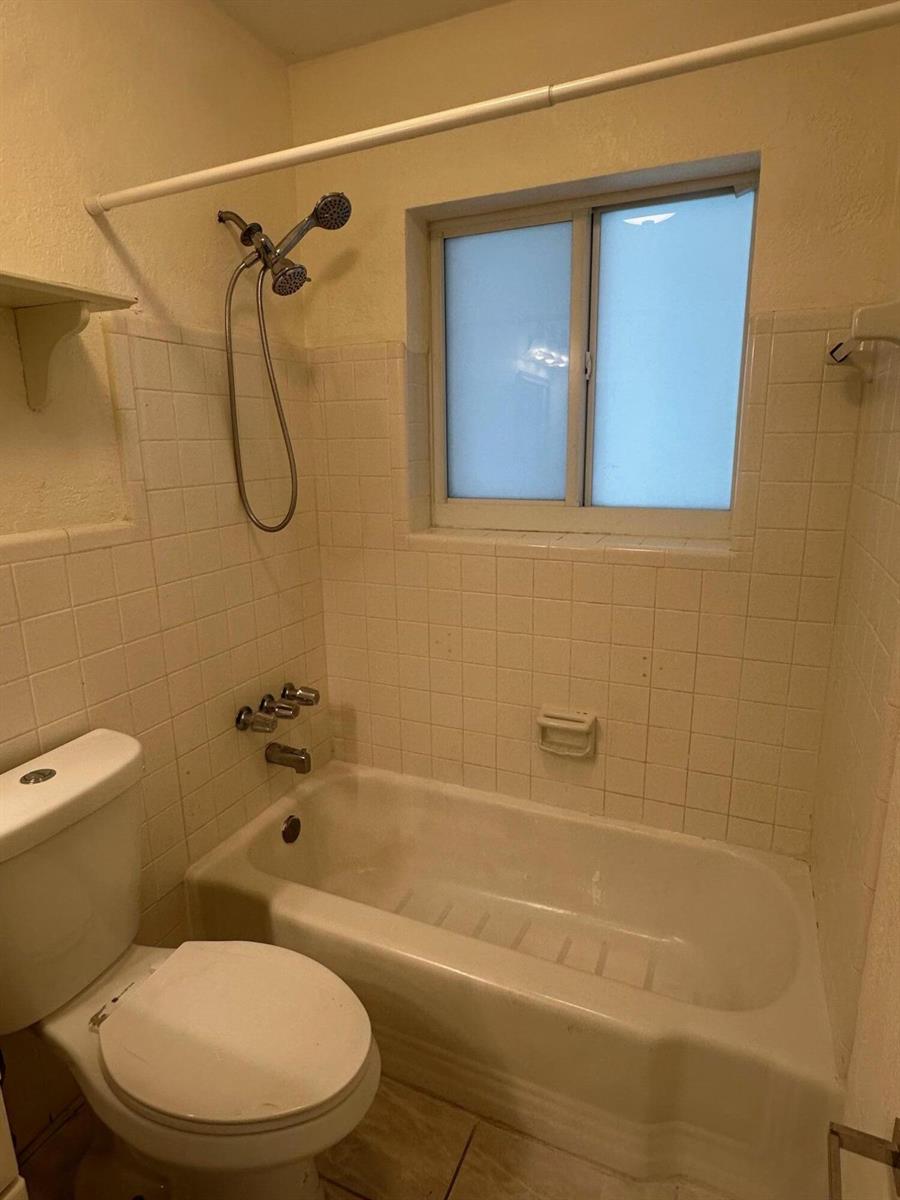 A bathroom features a white toilet, a bathtub with a showerhead, and tiled walls — 3850 NE 21st Way # 41, Lighthouse Point FL 33064, LIGHTHOUSE POINT, FL