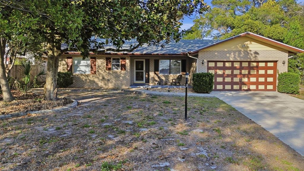 A single-story brick house with a two-car garage and a large tree in front — 244 ANGELES ROAD, DEBARY, FL