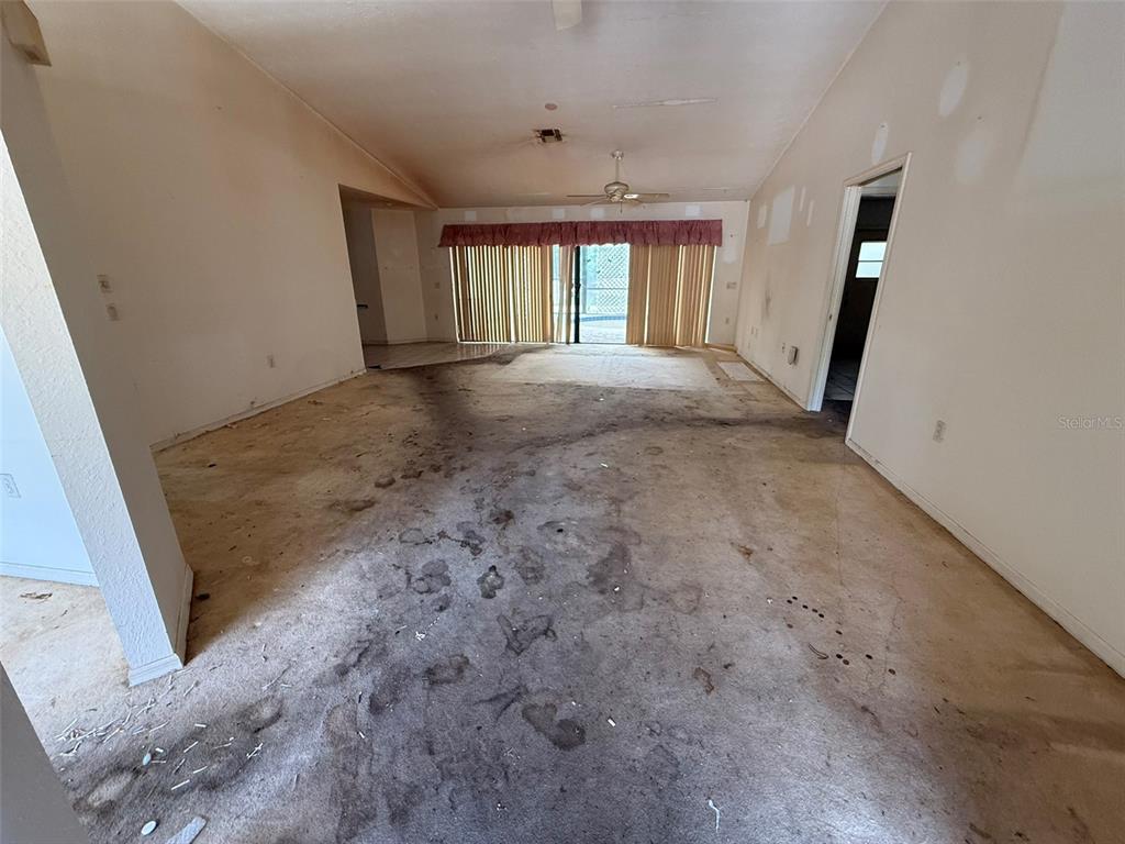 An empty living room features vaulted ceilings, a ceiling fan, and heavily stained wall-to-wall carpeting — 8548 CYPRESS LAKES BOULEVARD, NEW PORT RICHEY, FL
