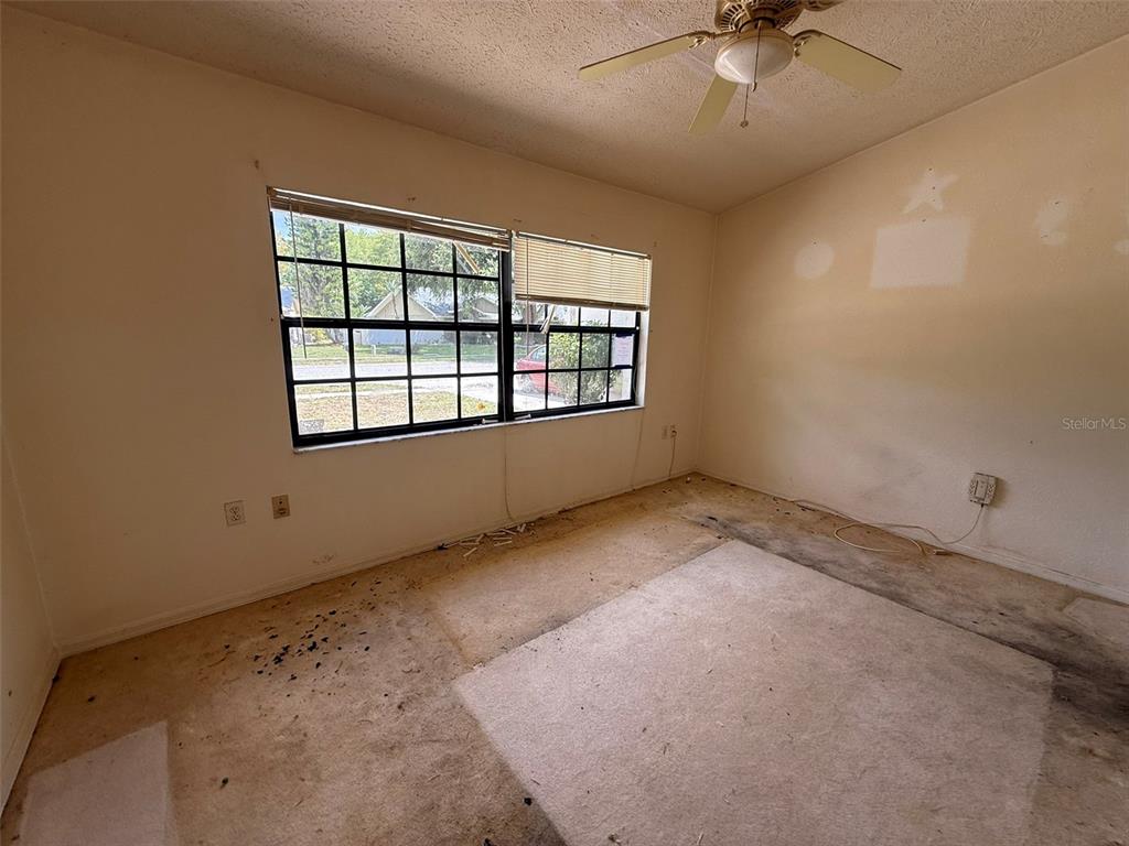 An empty bedroom features a ceiling fan, a multi-pane window, and worn, stained carpeting — 8548 CYPRESS LAKES BOULEVARD, NEW PORT RICHEY, FL