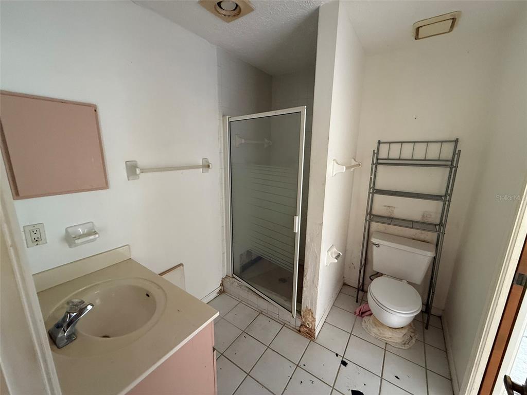 A bathroom features a vanity, a glass-enclosed shower, and a toilet with a metal shelf — 8548 CYPRESS LAKES BOULEVARD, NEW PORT RICHEY, FL