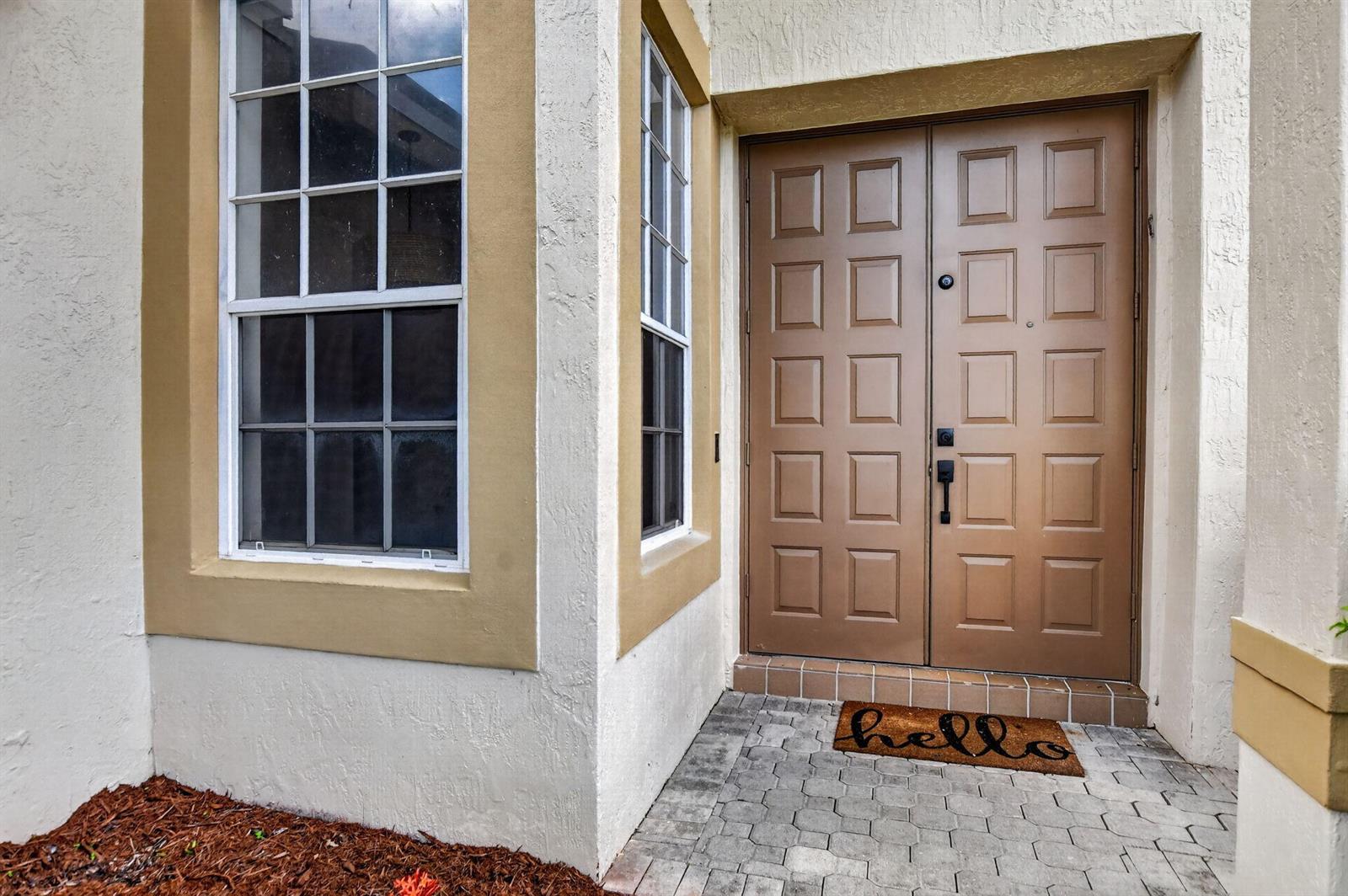 A brown double front door with a welcome mat sits beside a windowed wall — 18044 Jazz Lane, Boca Raton FL 33496, BOCA RATON, FL
