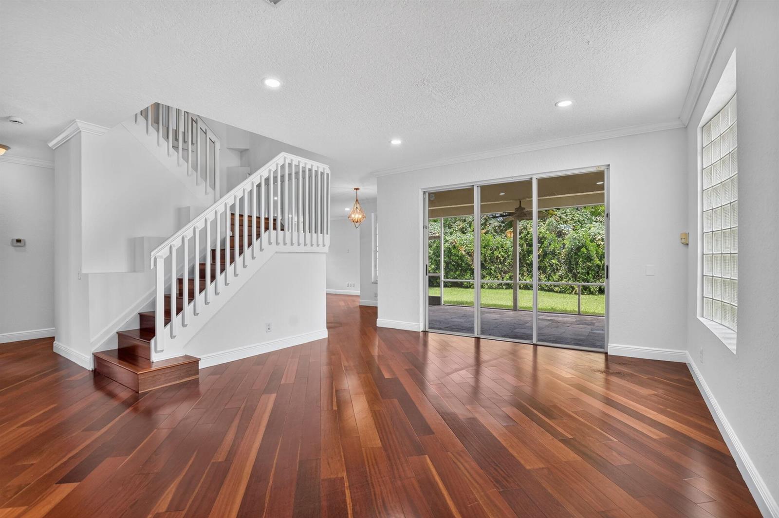 A living room with hardwood floors, a white staircase, and sliding glass doors to a patio — 18044 Jazz Lane, Boca Raton FL 33496, BOCA RATON, FL