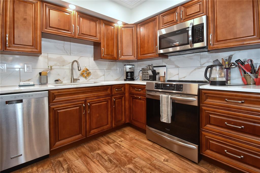A kitchen features wood cabinets, stainless steel appliances, and white marble-style backsplash tiles — 1503 CLOWER CREEK DRIVE UNIT HA262, SARASOTA, FL