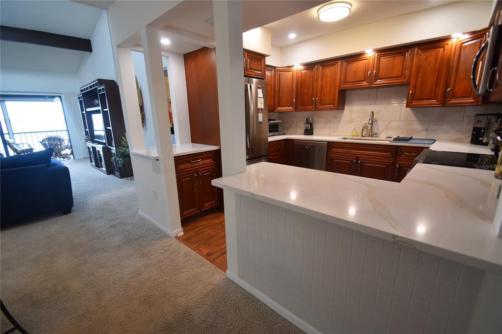 A kitchen with wood cabinets and white countertops overlooks a carpeted living area — 1503 CLOWER CREEK DRIVE UNIT HA262, SARASOTA, FL