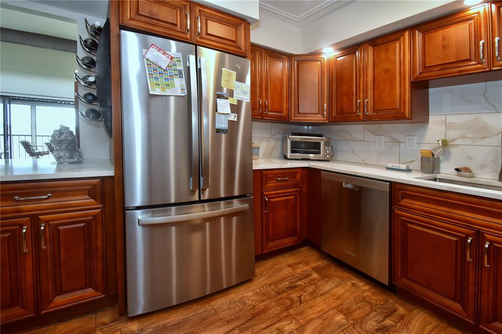 A kitchen features stainless steel appliances, wood cabinets, and white countertops with a tiled backsplash — 1503 CLOWER CREEK DRIVE UNIT HA262, SARASOTA, FL