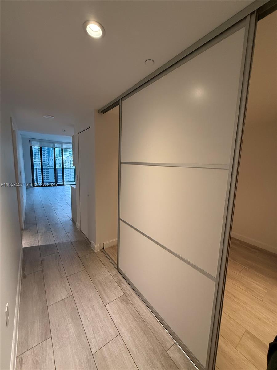 A hallway with wood-look tile flooring leads toward a room with floor-to-ceiling windows — 45 SW 9th St # 1004, Miami FL 33130, MIAMI, FL