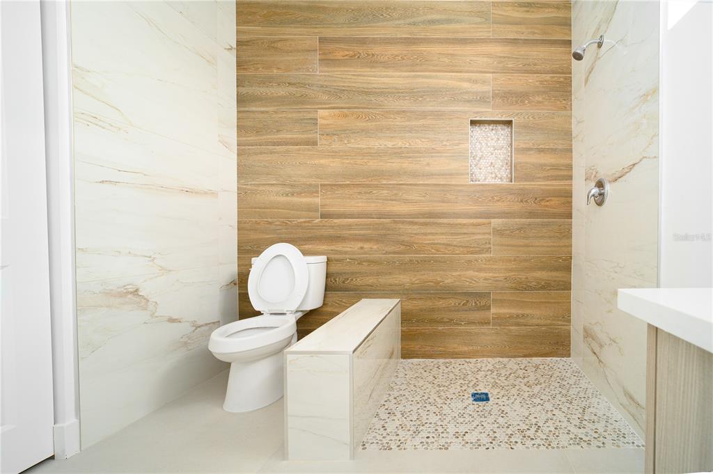A bathroom features a walk-in shower with pebble flooring, wood-look tile, and a white toilet — xx 15101 BRAINBRIDGE CIRCLE, PORT CHARLOTTE, FL