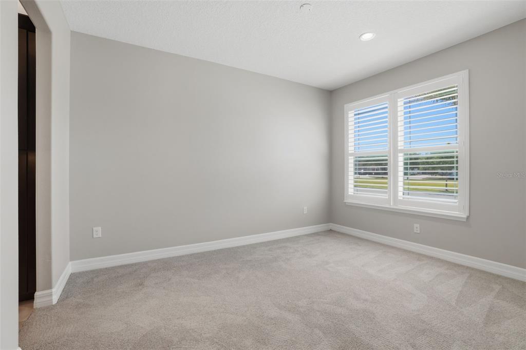 An empty bedroom features light gray walls, plush carpeting, and white plantation shutters — 10760 TIBBETT STREET, ORLANDO, FL