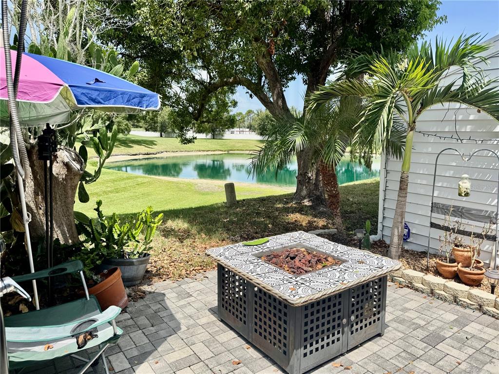 A patio features a square fire pit, a colorful umbrella, and a view of a pond — 3121 BEECHER DRIVE E UNIT D, PALM HARBOR, FL