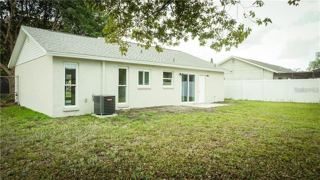 The rear exterior of a single-story house features a white stucco facade and lawn — 3409 VIDAL STREET, NEW PORT RICHEY, FL