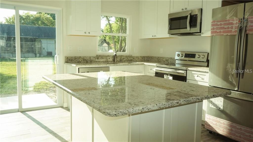A kitchen features white cabinets, granite countertops, a center island, and stainless steel appliances — 3409 VIDAL STREET, NEW PORT RICHEY, FL
