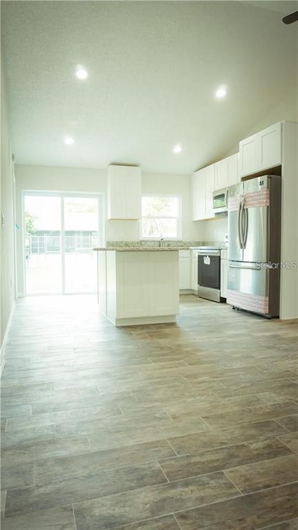 A kitchen with white cabinets, a center island, stainless steel appliances, and wood-look tile flooring — 3409 VIDAL STREET, NEW PORT RICHEY, FL