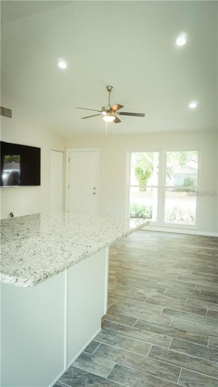 A kitchen island with a granite countertop overlooks a living area with wood-look tile flooring — 3409 VIDAL STREET, NEW PORT RICHEY, FL