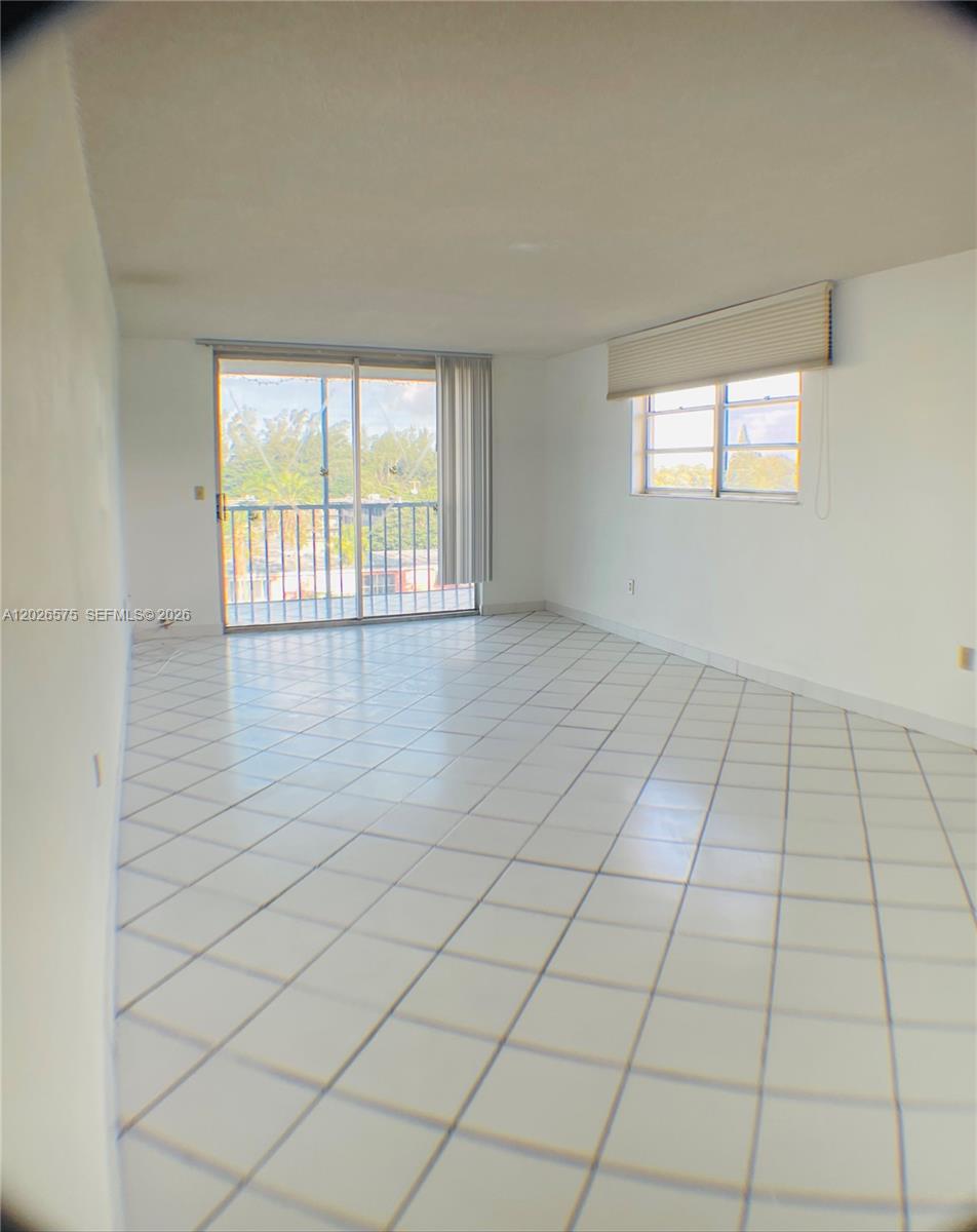 An empty room features white tiled floors, a sliding glass door, and a window — 12590 NE 16th Ave # 610, North Miami FL 33161, NORTH MIAMI, FL