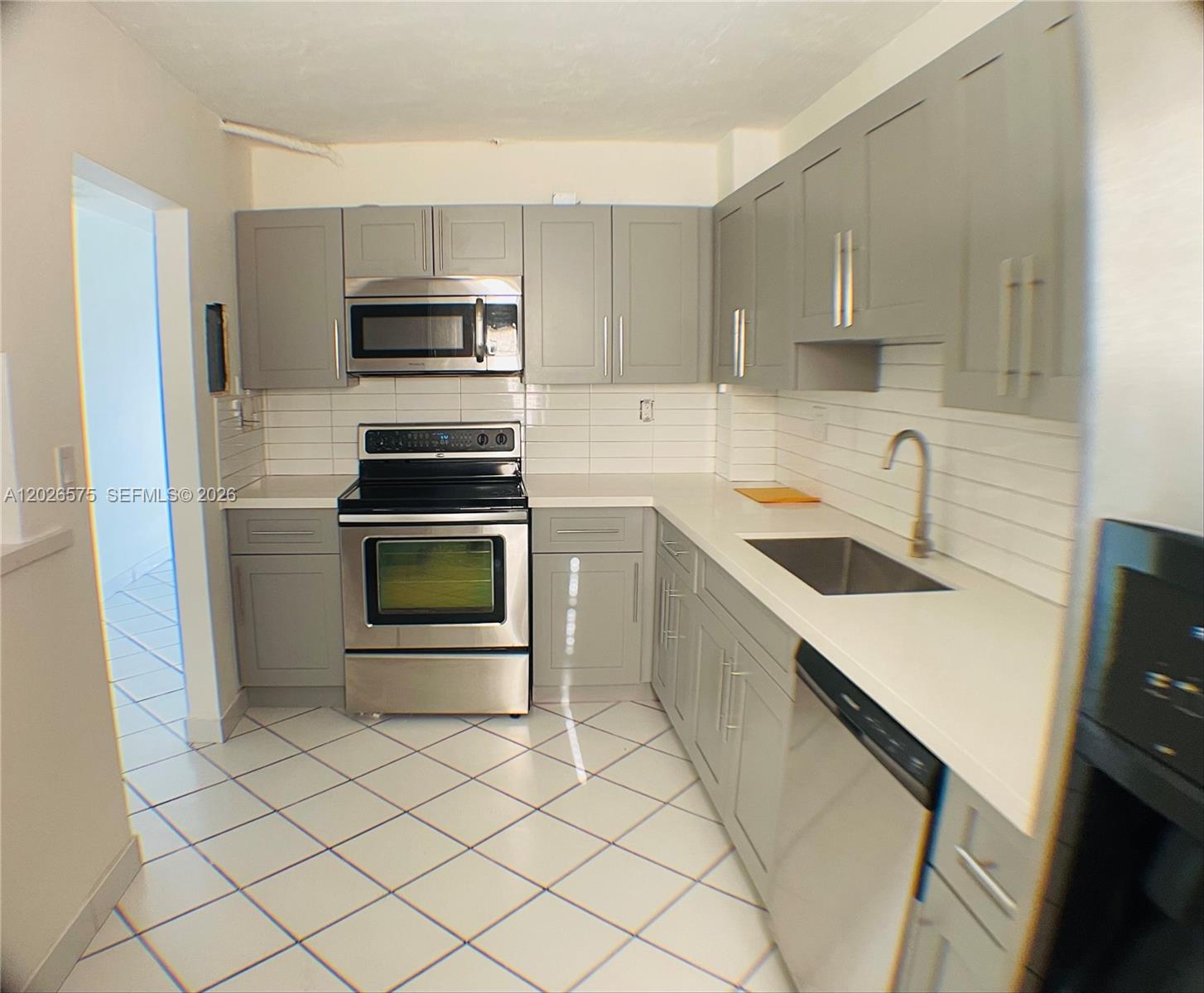 A kitchen features gray cabinets, white countertops, stainless steel appliances, and white tiled flooring — 12590 NE 16th Ave # 610, North Miami FL 33161, NORTH MIAMI, FL