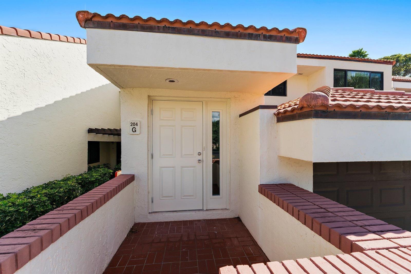 The exterior entrance features a white door, brick flooring, and a terracotta-tiled roof — 204 Sea Oats Drive # G, Juno Beach FL 33408, JUNO BEACH, FL