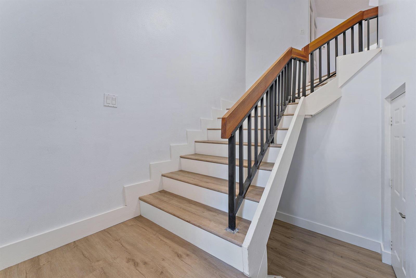 A staircase with wood-look treads, white risers, and a black metal railing with a wood handrail — 204 Sea Oats Drive # G, Juno Beach FL 33408, JUNO BEACH, FL