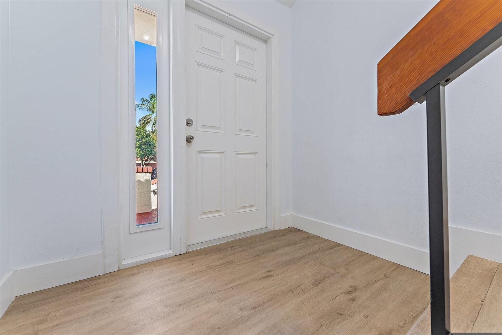 An entryway features light wood-look flooring, a white door with a sidelight, and a staircase — 204 Sea Oats Drive # G, Juno Beach FL 33408, JUNO BEACH, FL