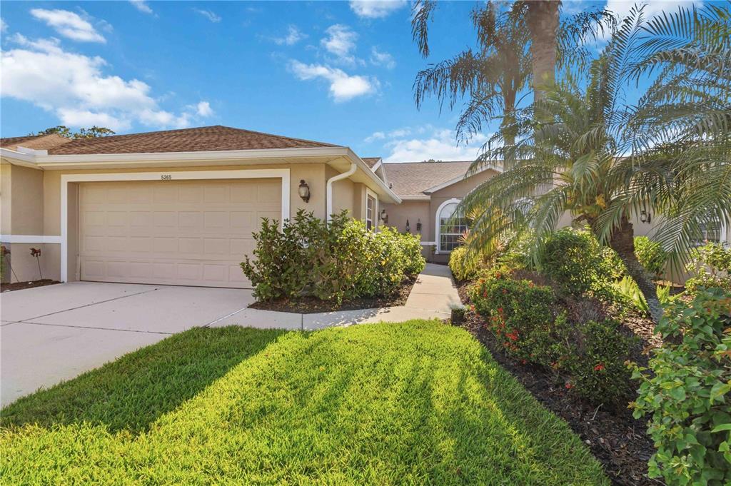 A single-story house with a beige stucco exterior, a two-car garage, and landscaped front yard — 5265 CHASE OAKS DRIVE, SARASOTA, FL
