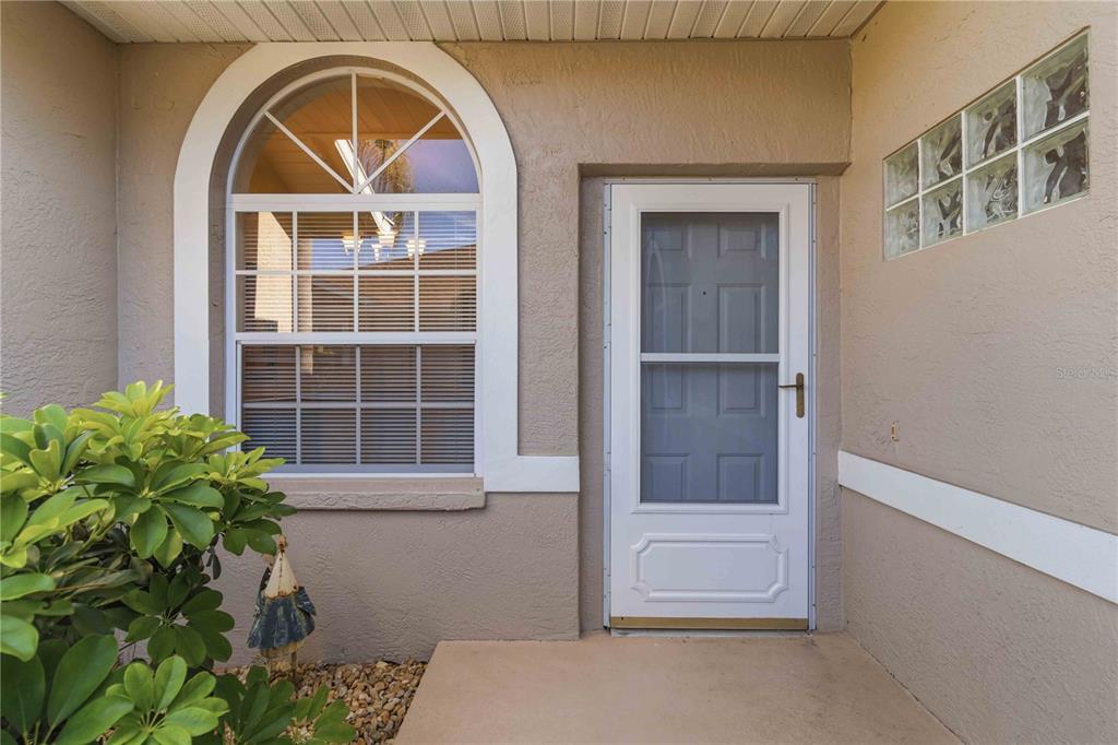 A beige exterior wall features a white storm door, an arched window, and glass blocks — 5265 CHASE OAKS DRIVE, SARASOTA, FL