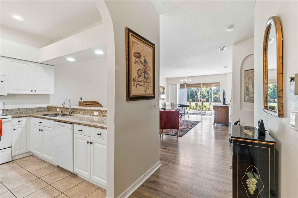 A kitchen with white cabinets and granite countertops opens into a living area with flooring — 5265 CHASE OAKS DRIVE, SARASOTA, FL