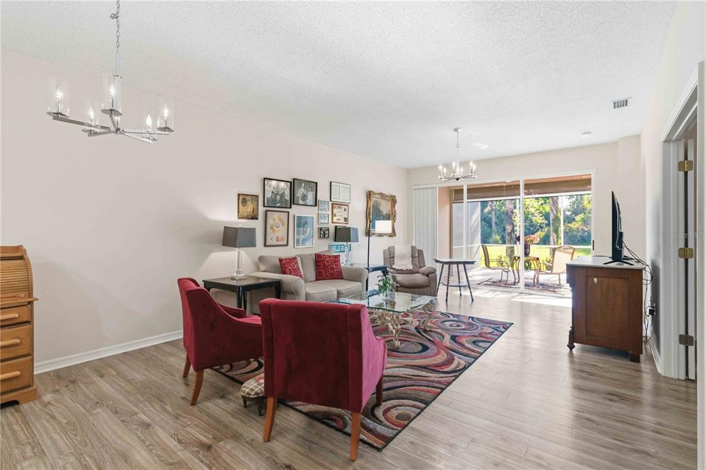 A living room with wood-look flooring, red armchairs, a sofa, and a sliding glass door — 5265 CHASE OAKS DRIVE, SARASOTA, FL