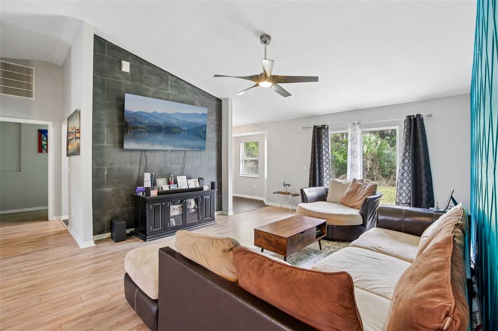 A living room features a dark tiled accent wall with a mounted television and wood flooring — 4628 ADDERTON AVENUE, NORTH PORT, FL