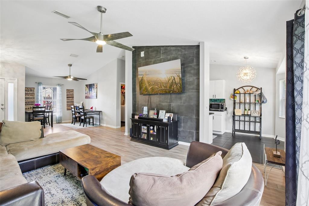 A living room with a dark tiled accent wall, a mounted television, and ceiling fans — 4628 ADDERTON AVENUE, NORTH PORT, FL