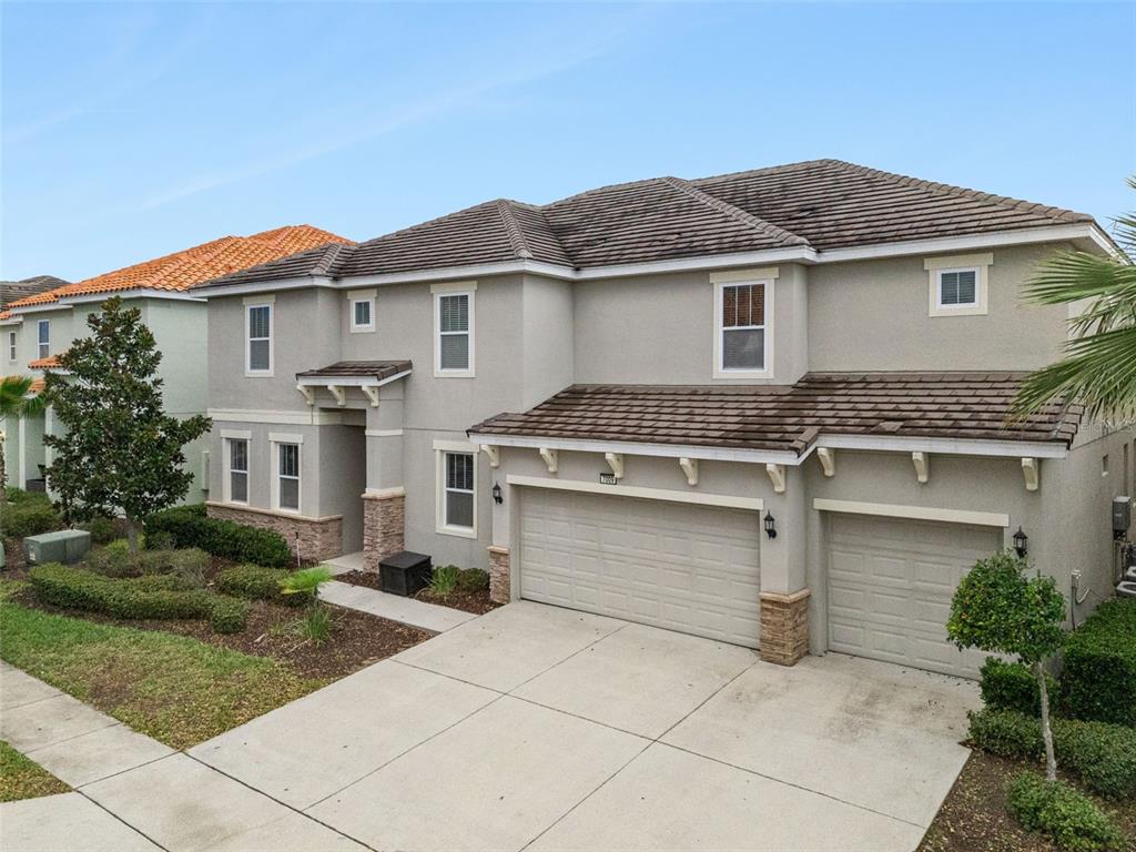 A two-story suburban house with a beige stucco exterior, tile roof, and three-car garage — 7009 OAKWOOD STREET, DAVENPORT, FL