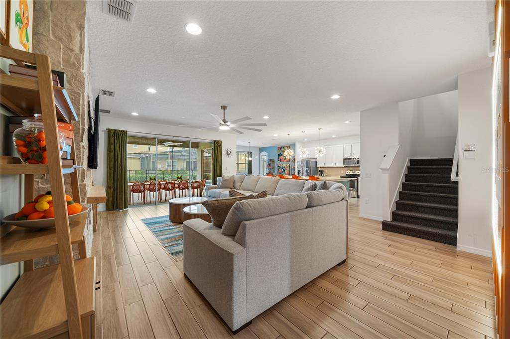 A spacious living room with light wood floors, a large sectional sofa, and stairs — 7009 OAKWOOD STREET, DAVENPORT, FL