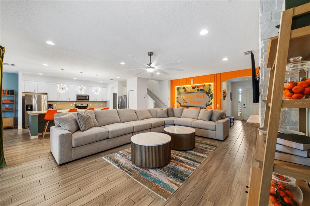 A spacious open-concept living room features a large sectional sofa, two round coffee tables, and orange accents — 7009 OAKWOOD STREET, DAVENPORT, FL
