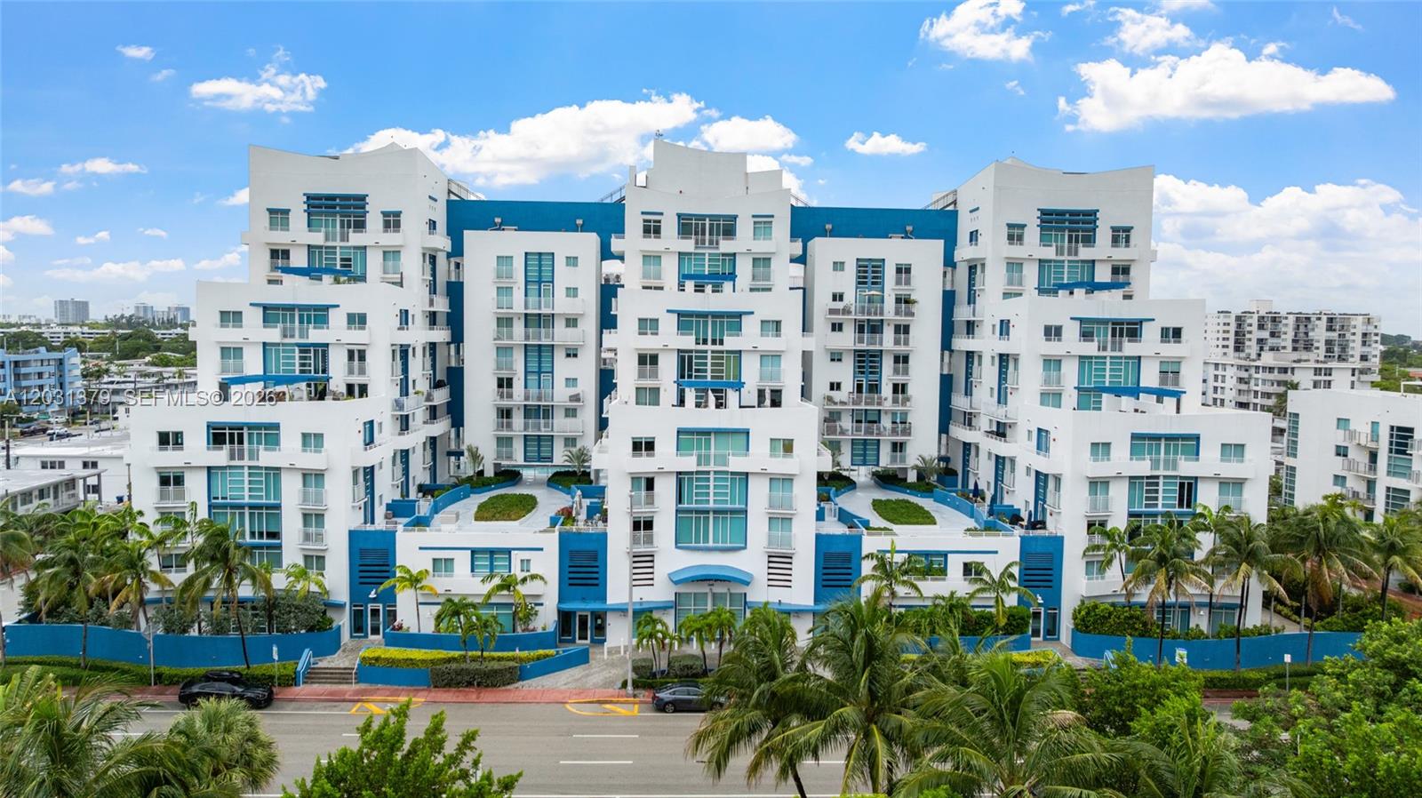 A multi-story white and blue apartment building with palm trees and a street in front — 7600 Collins Ave # 1210, Miami Beach FL 33141, MIAMI BEACH, FL