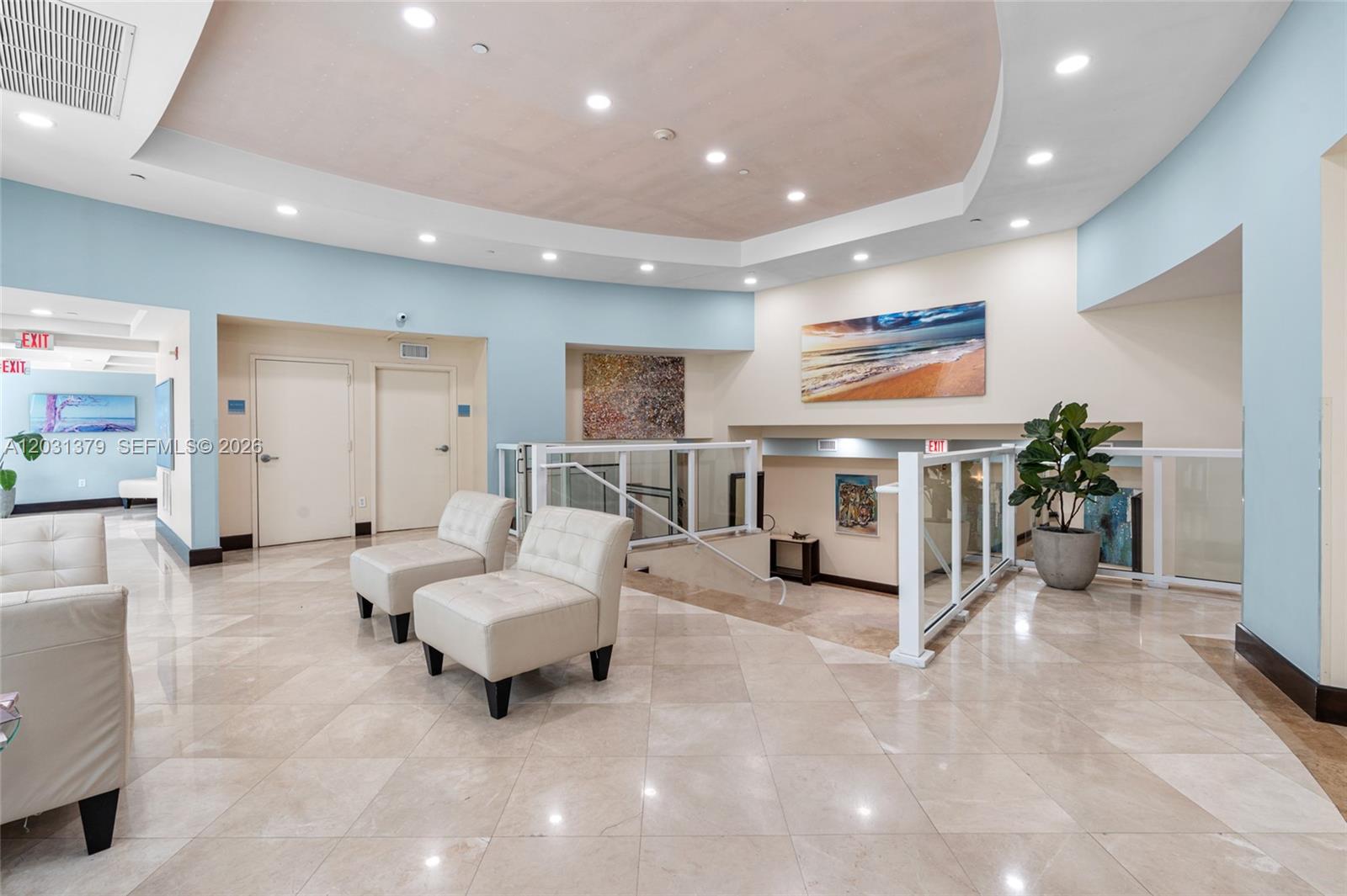 A bright lobby features light-colored tile floors, two white chairs, and a staircase with railings — 7600 Collins Ave # 1210, Miami Beach FL 33141, MIAMI BEACH, FL