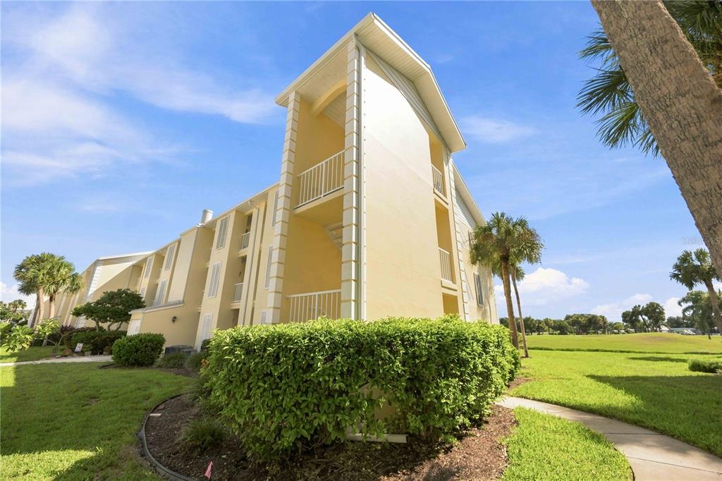 A multi-story yellow apartment building stands on a grassy lawn with palm trees — 406 CERROMAR CIRCLE N UNIT 328, VENICE, FL