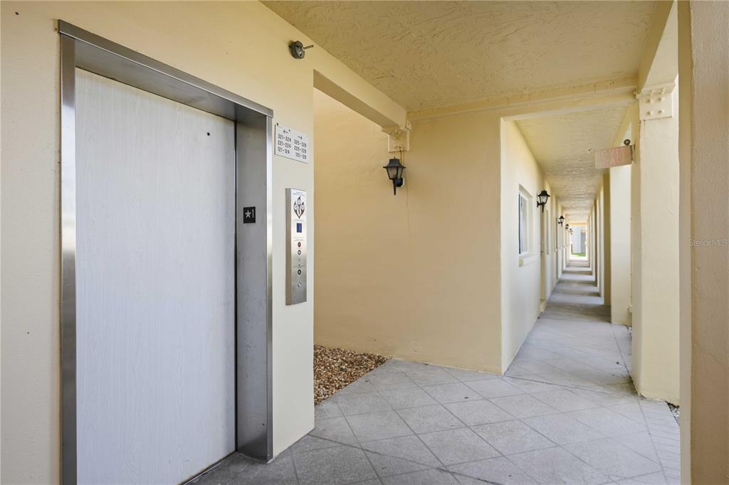 An elevator door and a long, covered outdoor walkway with light-colored walls and tile flooring — 406 CERROMAR CIRCLE N UNIT 328, VENICE, FL