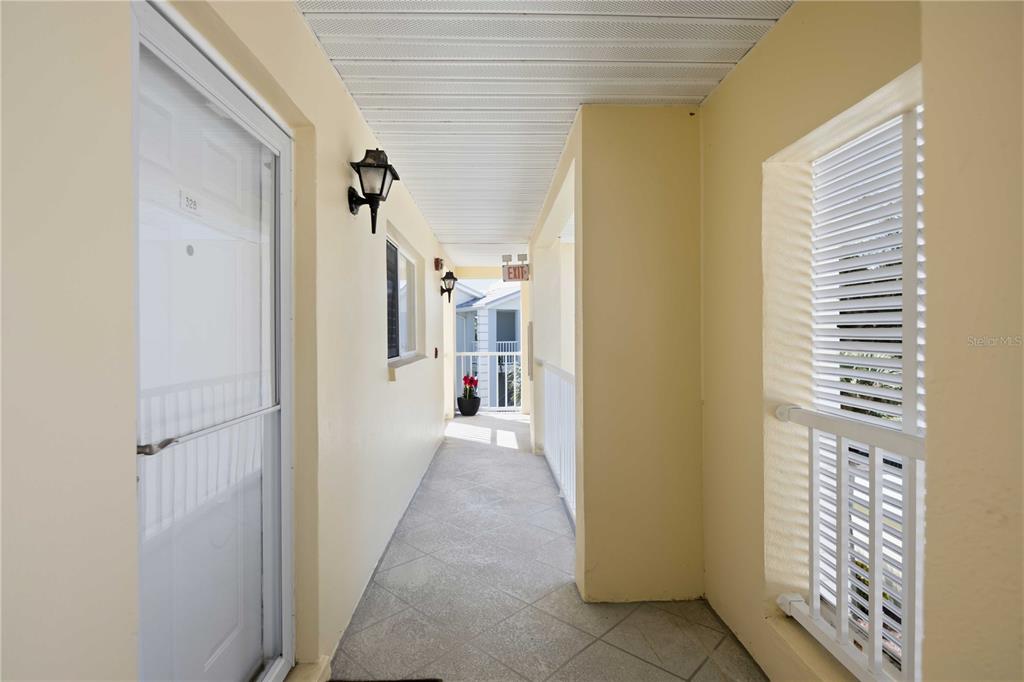 An outdoor apartment hallway with light-colored walls, tiled flooring, and a white railing — 406 CERROMAR CIRCLE N UNIT 328, VENICE, FL