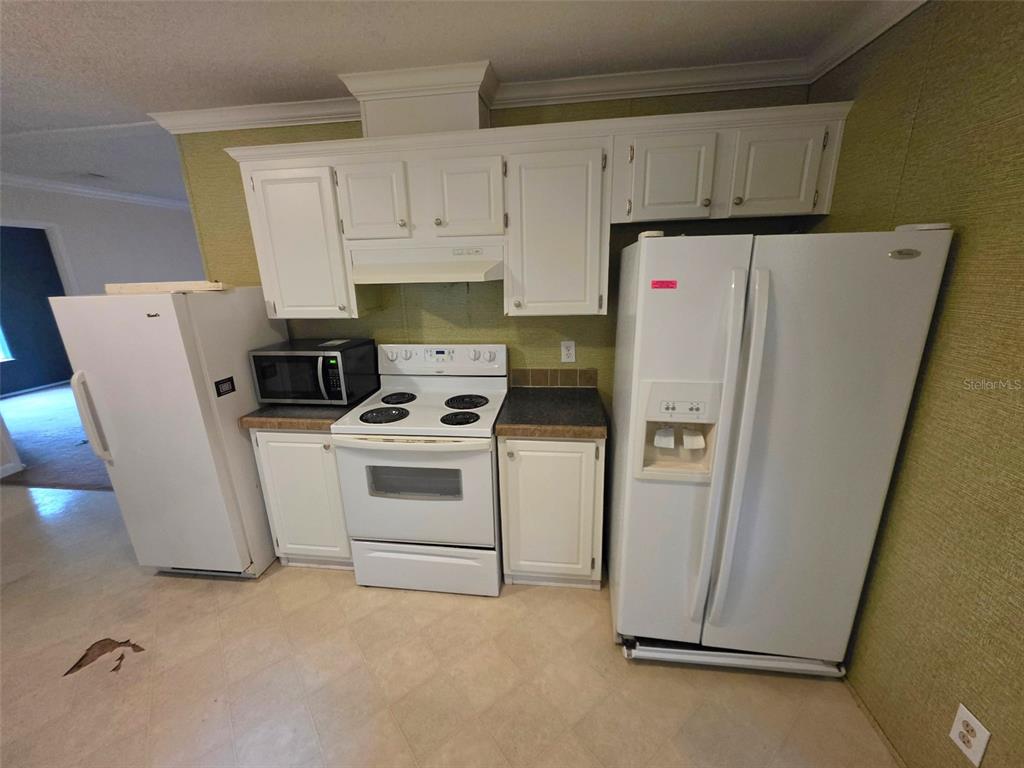 A kitchen features white appliances, white cabinets, and green textured wallpaper — 14263 ANNUTALAGA AVENUE, BROOKSVILLE, FL