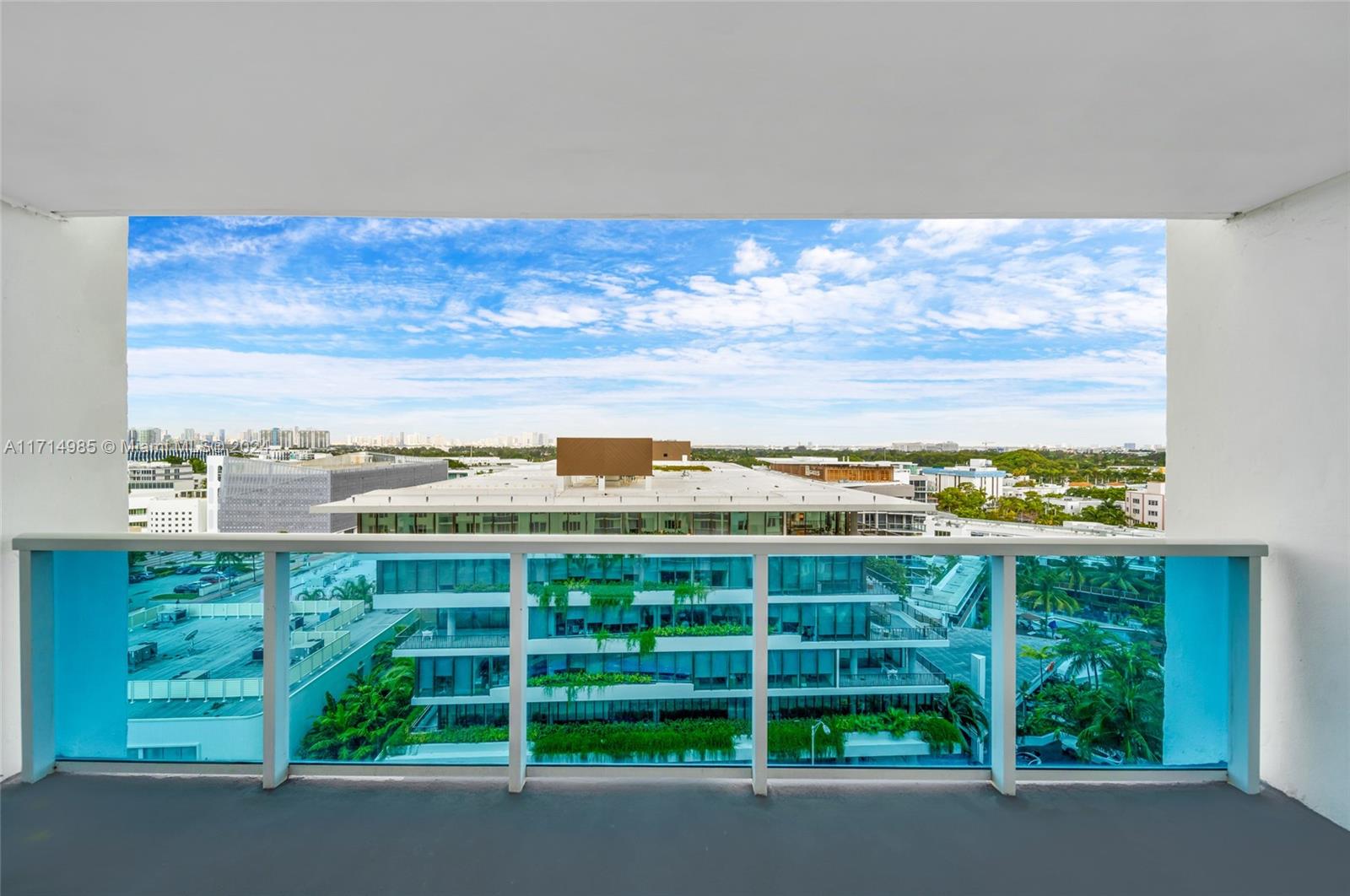 A balcony with a blue glass railing overlooks a modern building and urban landscape — 2301 Collins Ave # 1030, Miami Beach FL 33139, MIAMI BEACH, FL